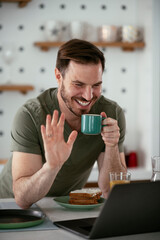 Handsome man drinking coffee in kitchen. Young man having video call.