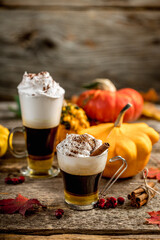 Pumpkin spice latte with cinamon powder and delicious flavours on the old textured wood table with colorful dry leaves and pumpkins