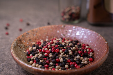 The beautiful spice blend is comprised of black, red, green, and white peppercorns in a small bowl  on rustic table