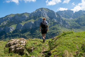 Fototapeta na wymiar Junger Mann mit Rucksack blickt auf Berggipfel Panorama in Appenzell, Schweiz