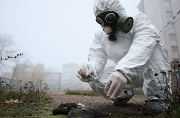 Man in gas mask and protective clothing monitoring abandoned football pitch in emty city, fog...