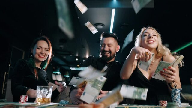 Two young women and bearded man are winning and rejoice in victory at the casino and throw money in the air