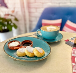 curd cakes with sour cream and jam on a blue plate, a cup of coffee on the table. delicious breakfast in a cafe