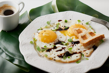 Morning breakfast with fried eggs ,toast and coffee in white cup and plant leaf on white table