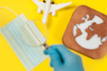 Plane model, face mask, loupe in hand and earth model on a yellow background. Flight impact of coronavirus (COVID-19) concept..