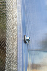 Steel hex bolt on the wall of a polycarbonate plastic greenhouse close up