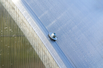 Steel hex bolt on the wall of a polycarbonate plastic greenhouse close up
