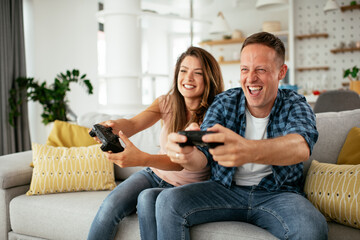Husband and wife playing video game with joysticks in living room. Loving couple are playing video...