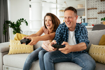 Husband and wife playing video game with joysticks in living room. Loving couple are playing video games at home.
