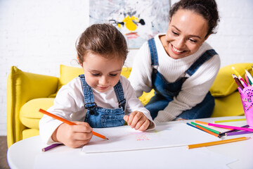 Daughter drawing with color pencils near mother at home