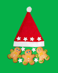 Three gingerbread men and a Santa Claus hat are located on a green background. New Year and Christmas concept