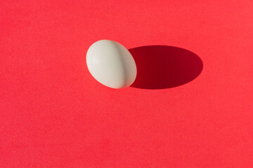Fototapeta na wymiar White egg on a red background. There is a clear shadow. Template, graphic resource