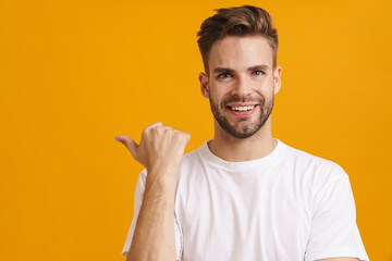 Joyful handsome unshaven guy smiling and pointing finger aside