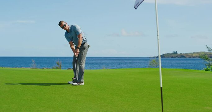Man playing golf on beautiful course by the ocean, putting on the green into the hole
