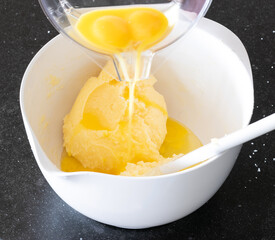 Mixing eggs with butter sugar creamy dough in a white bowl for cup cakes, following a recipe