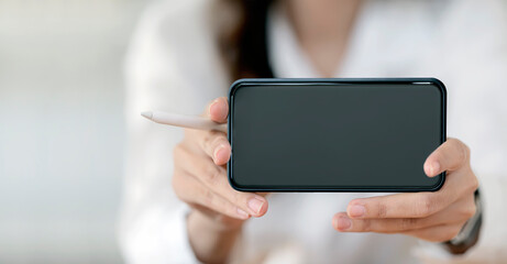 Closeup view of female hands showing blank screen smartphone in horizontal view, copy space.