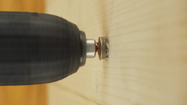 Self-tapping screw in a wooden wall. Screwdriver screw lag bolt. Electric drill screws the lag bolt in a wooden surface, vertical close-up view.