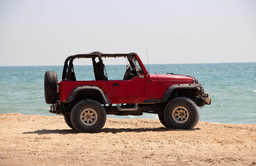 Fototapeta na wymiar Red car on the sandy seashore. Summer vacation at the sea.
