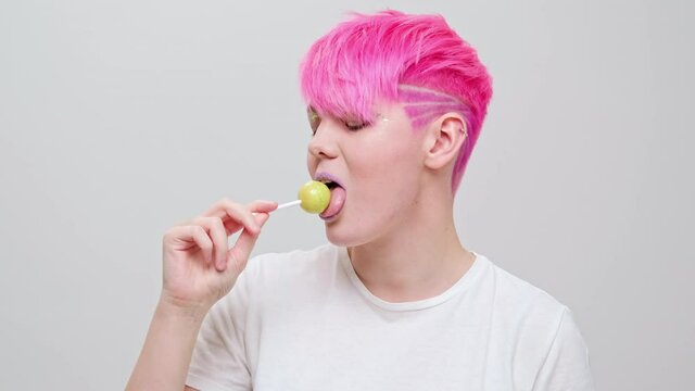 Young beautiful girl with a short haircut and pink hair. A homosexual lesbian model poses on a white background in the studio.