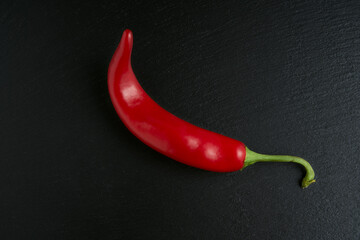 Isolated red hot chili pepper on black stone background, ideal ingredient for spicy and passionate...