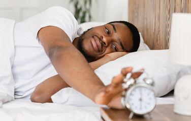 Wellslept Black Man Turning Off Alarm-Clock Waking Up In Bedroom - obrazy, fototapety, plakaty