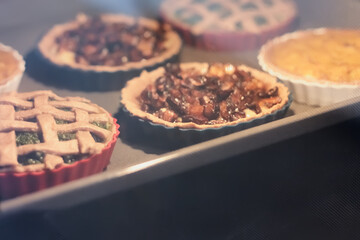 Homemade savory mini tarts or quiche pies with mushrooms, pumpkin and spinach baking in electric oven. Production oven at the bakery. View through glass oven door. Selective focus