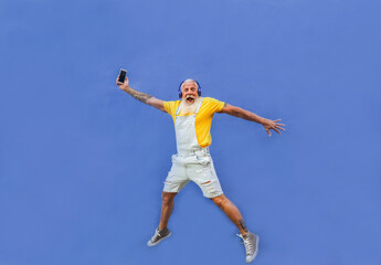 Fototapeta na wymiar Cheerful hipster man jumping - Happy senior with smartphone and headphones enjoy music from playlist - Technology