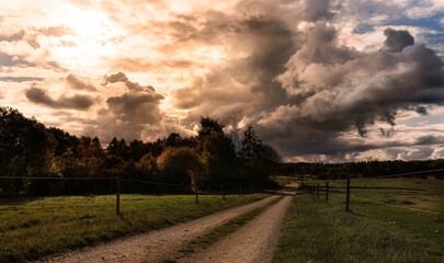 Dramatic sky with dark clouds over pastures with gravel road