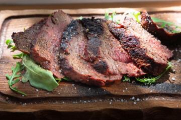 Medium rare baked veal with coarse salt, spices and arugula leaves on wooden background