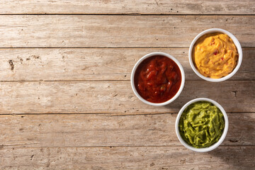 Traditional Mexican sauces. Guacamole, chilli pepper sauce and cheese sauce on wooden table