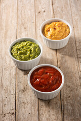 Traditional Mexican sauces. Guacamole, chilli pepper sauce and cheese sauce on wooden table