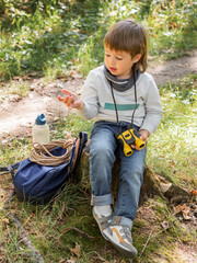 Little explorer on hike in forest. Boy with binoculars and compass sits on stump and reads map. Outdoor leisure activity for children. Summer journey for young tourist.