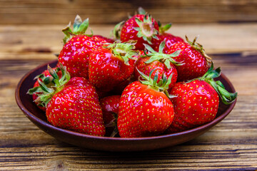 Ceramic plate with pile of ripe strawberries on wooden table