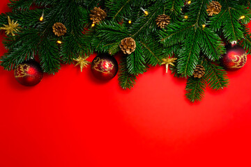 view from above on Fir branches decorated with red Christmas Ball Baubles, String Lights, golden stars and pine cones on red background with copy space. Xmas or New Year greeting card.