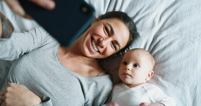 Authentic close up of neo mother and her newborn baby making a selfie or video call to father or relatives in a bed.