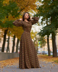 Elegant caucasian brunette woman with long wavy hair in long brown dress with floral print walking...