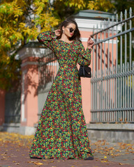 Elegant caucasian brunette woman with long wavy hair in long green dress with floral print walking...