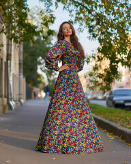 Elegant caucasian brunette woman with long wavy hair in long colorful dress with floral print...
