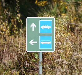 A traffic sign showing parking direction for car and buses with forest in background