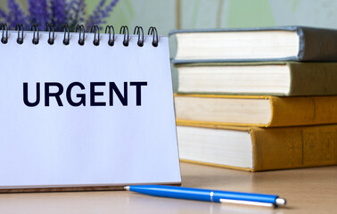 URGENT - a word in a notebook against the background of old books with a pen