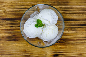 Glass bowl with ice cream balls and mint leaf on a wooden table. Top view
