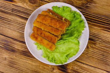 Baked fish sticks and lettuce leaves in a plate. Top view