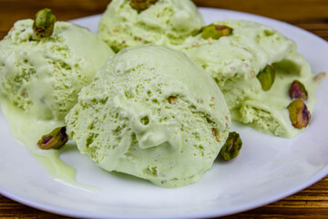 Glass bowl with pistachio ice cream balls and nuts on a wooden table