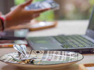 Closeup of blank ceramic plate with blurry notebook, woman 's hand and mobile phone background in house, cafe or office for working or studying from home concept.