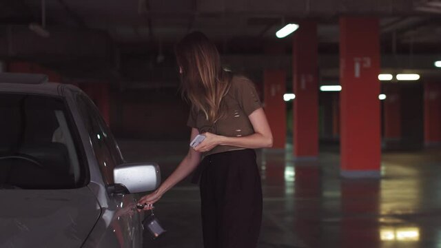 An attractive woman uses a key to open a car in an underground parking lot. A good-looking girl opens the car.