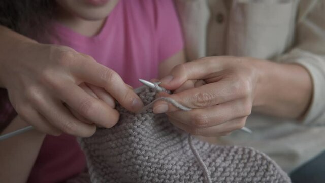 Knit together. A view of female and little girl's hands knitting a grey wool in the room.
