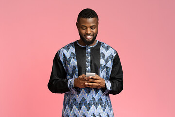 Smiling black guy using smartphone, wearing african t-shirt