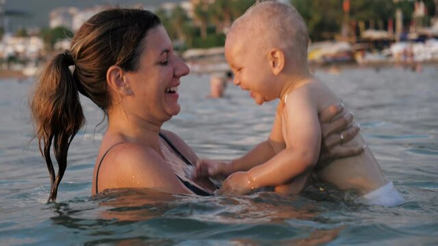 Funny Smiling Caucasian Woman Mother Playing With Baby Swimming In Sea At Resort