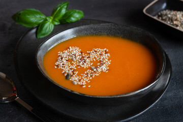 Close-up photo of plate with fresh homemade pumpkin cream soup with seeds and basil on dark background