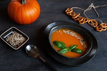 Close-up photo of plate with fresh homemade pumpkin cream soup with seeds and basil on dark background